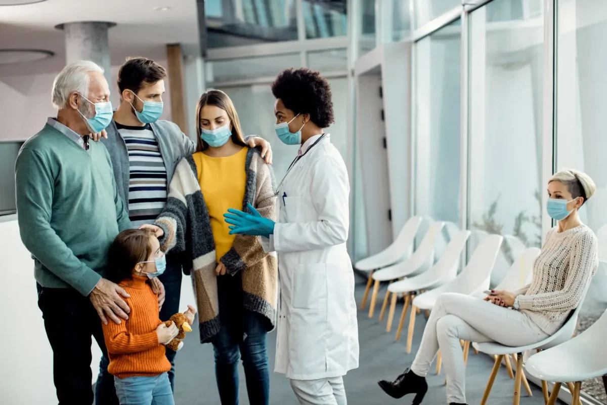 Doctor consulting masked family in clinic waiting room